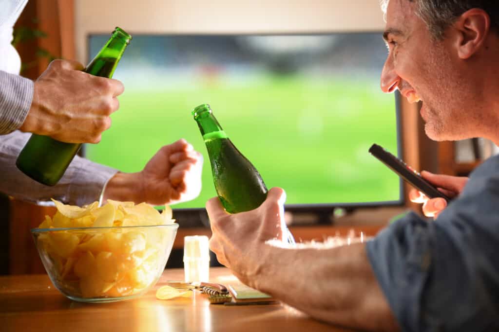 dois amigos assistindo a jogos juntos enquanto comem e tomam cerveja