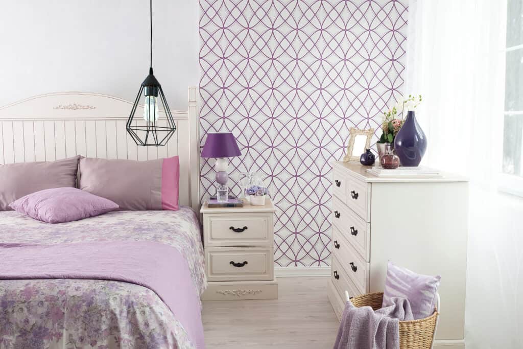 um quarto com o tema roxo e branco, a decoração com papel de parede é feita com esses tons em uma estampa moderna e cheia de personalidade