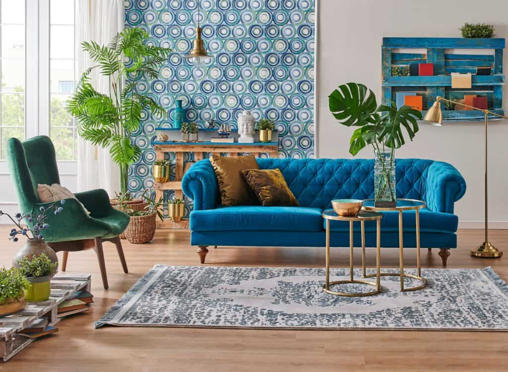 papel de parede para sala em azul e branco, na imagem tem ainda uma sala com algumas plantas, um sofá, uma poltrona, tapete e algumas mesas e prateleiras