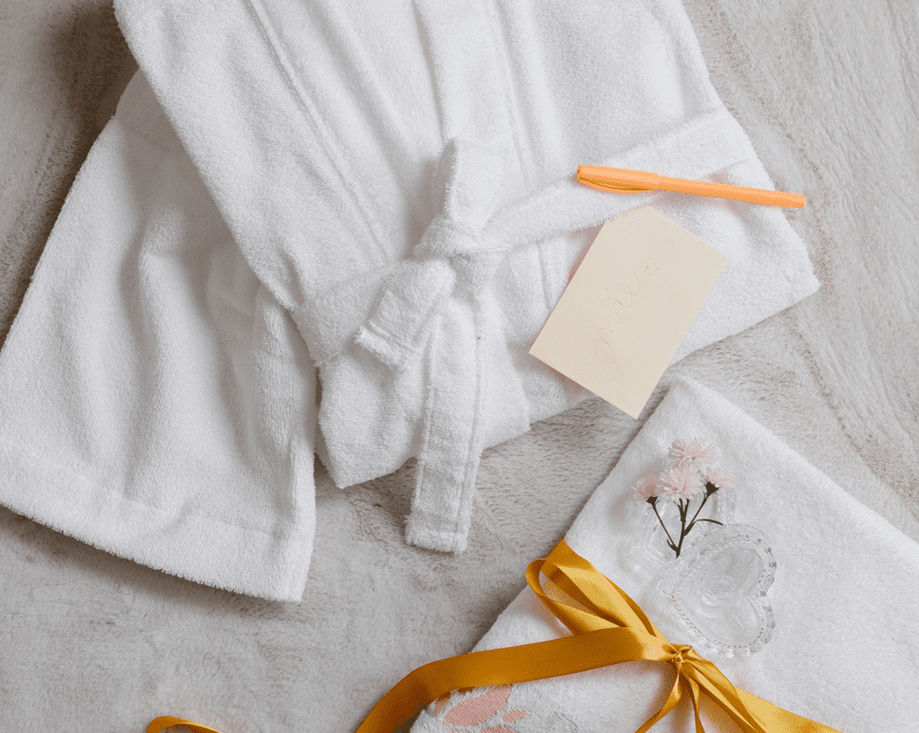 imagem com roupão, papel, toalhas e uma caneta, dando a ideia de presente para mãe que gosta de relaxar