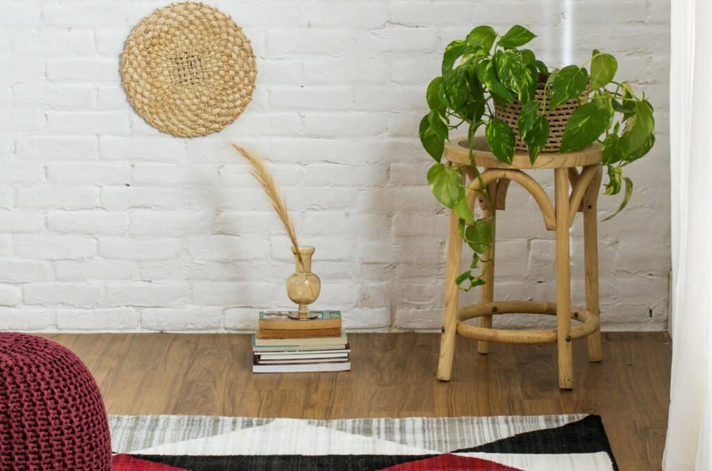um cantinho da sala com livros no chão, um banco com uma planta em cima, um tapete e um puff