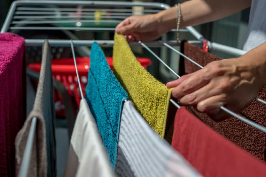 varal que mostra como lavar toalhas de banho e a melhor forma de colocar as peças coloridas e brancas longe do sol, uma mão pendura uma toalha em um varal com várias outras