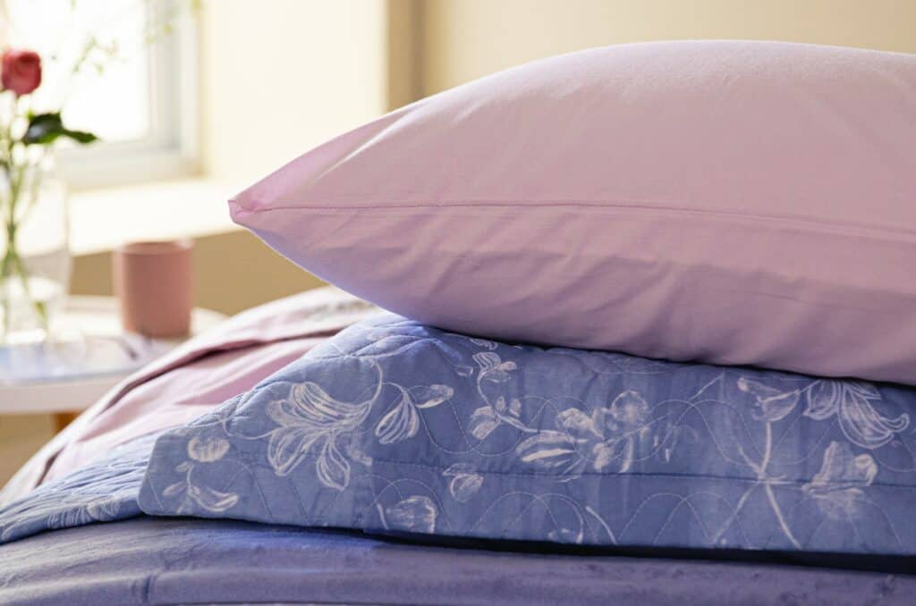 dois travesseiros perfeitos para fazer uma cama posta digna de novela, um deles é liso em rosa claro e o outro possui delicada estampa floral em branco com fundo azul
